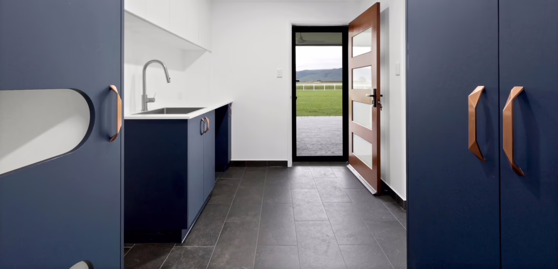 Modern navy and white laundry with copper handles and outdoor access by NV Builders Mackay